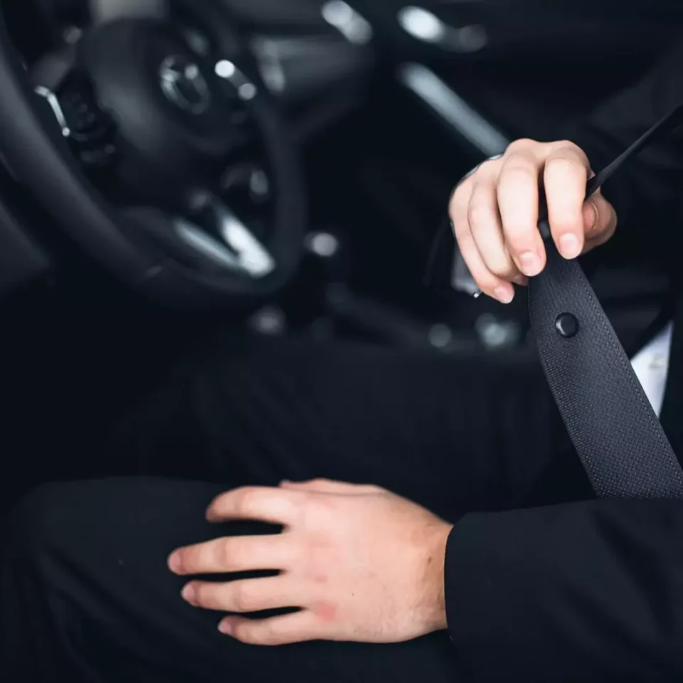 close up of the inside of a car, driving wheel and person putting the seatbelt